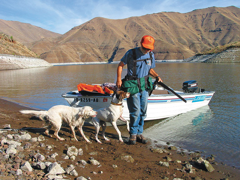 chukar hunter with 2 dogs by water