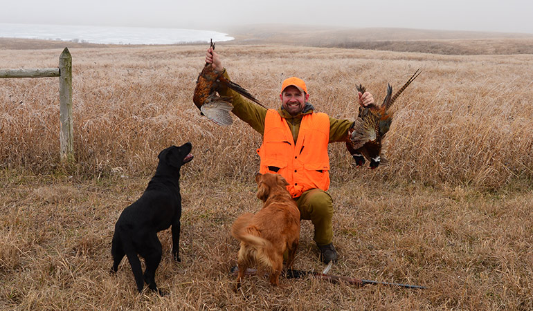 Tony Peterson holding roosters with 2 retrievers