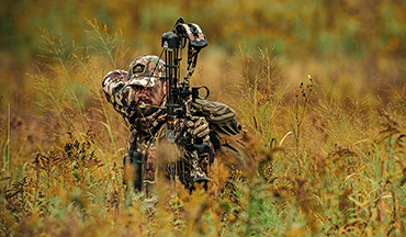 Bowhunter at full draw in tall grass