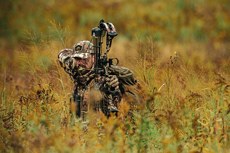 Bowhunter at full draw in tall grass