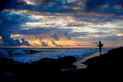 angler fishing on a windy beach at sunrise