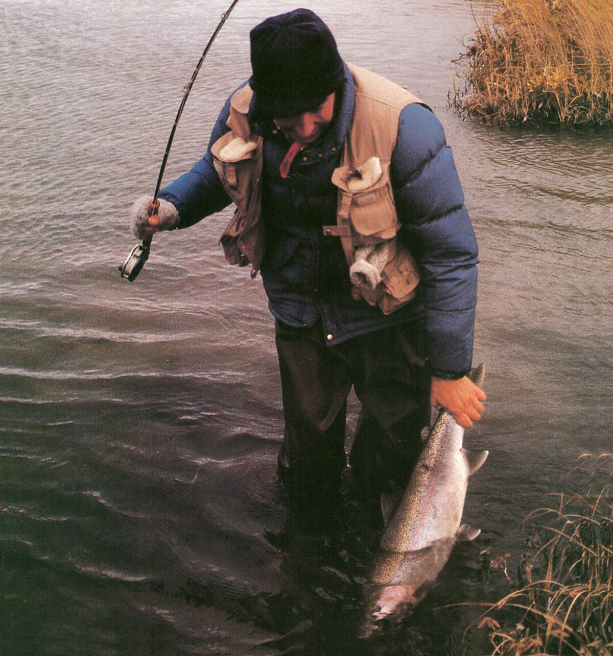 Adult stands in shallow and holding fly rod in hands. He is fishing. Guy is  holding