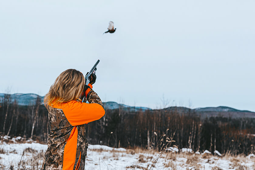 Female hunter shooting a ring-necked pheasant rooster