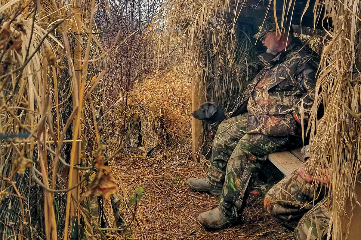 a duck hunter sitting in a duck corral with a black labrador