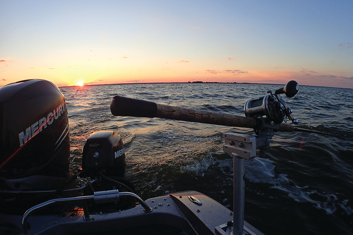 A trolling rod mounted on a boat on a lake at dusk