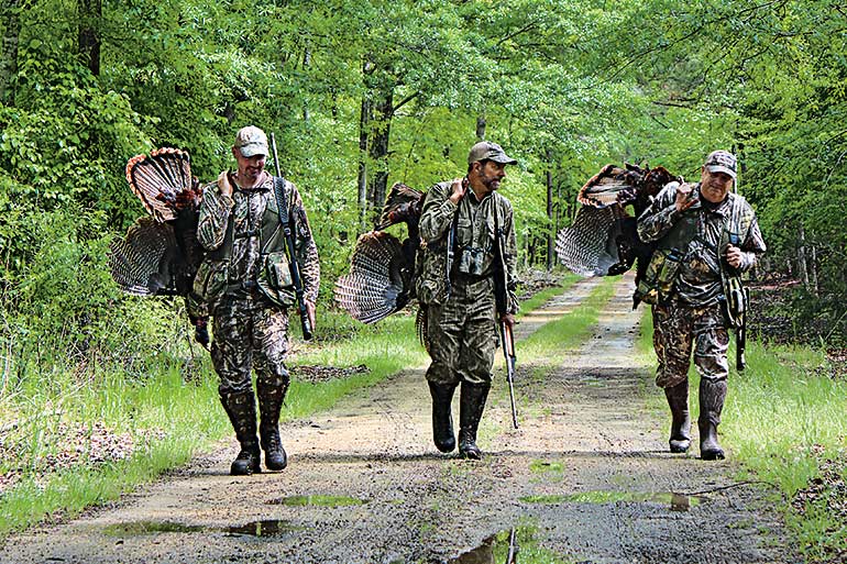 three hunters carrying turkeys