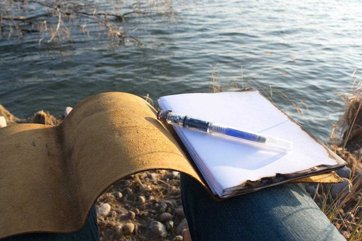 leather-bound notebook open on lap near waters edge