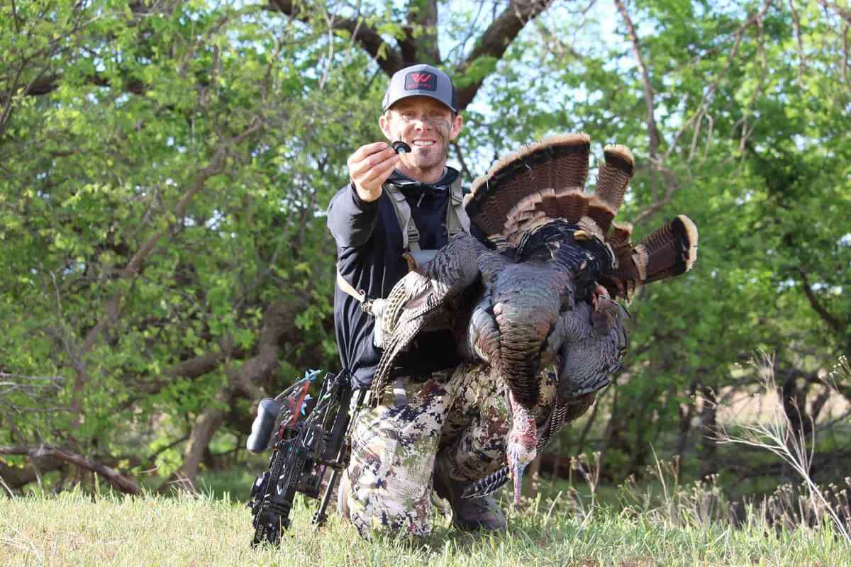 bowhunter with downed turkey holding mouth call