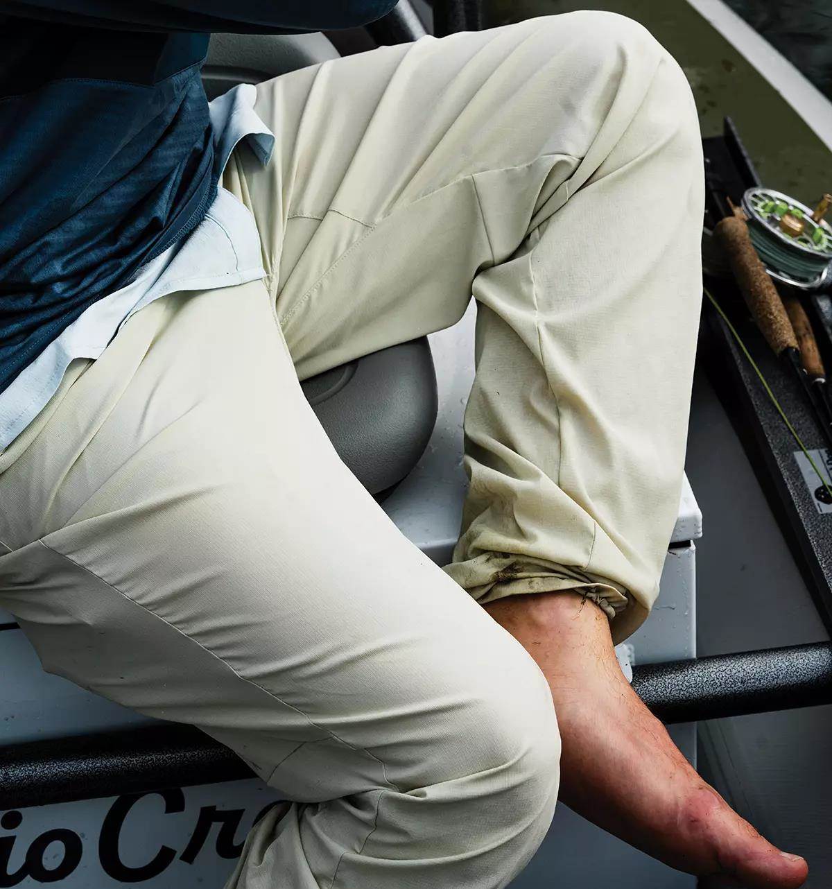 A closeup of a man's pants as he sits in a drift boat next to a couple of fly rods.
