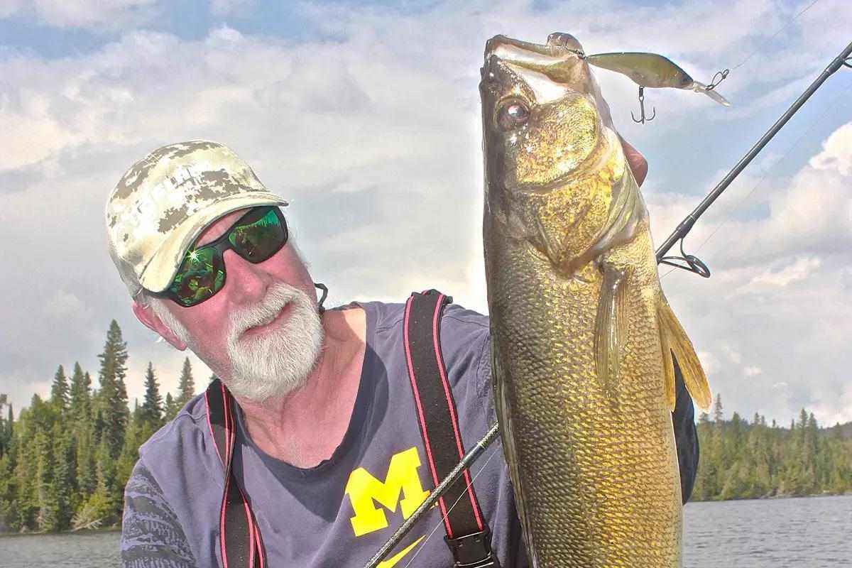 An angler holds up a caught walleye with the lake in the background. 