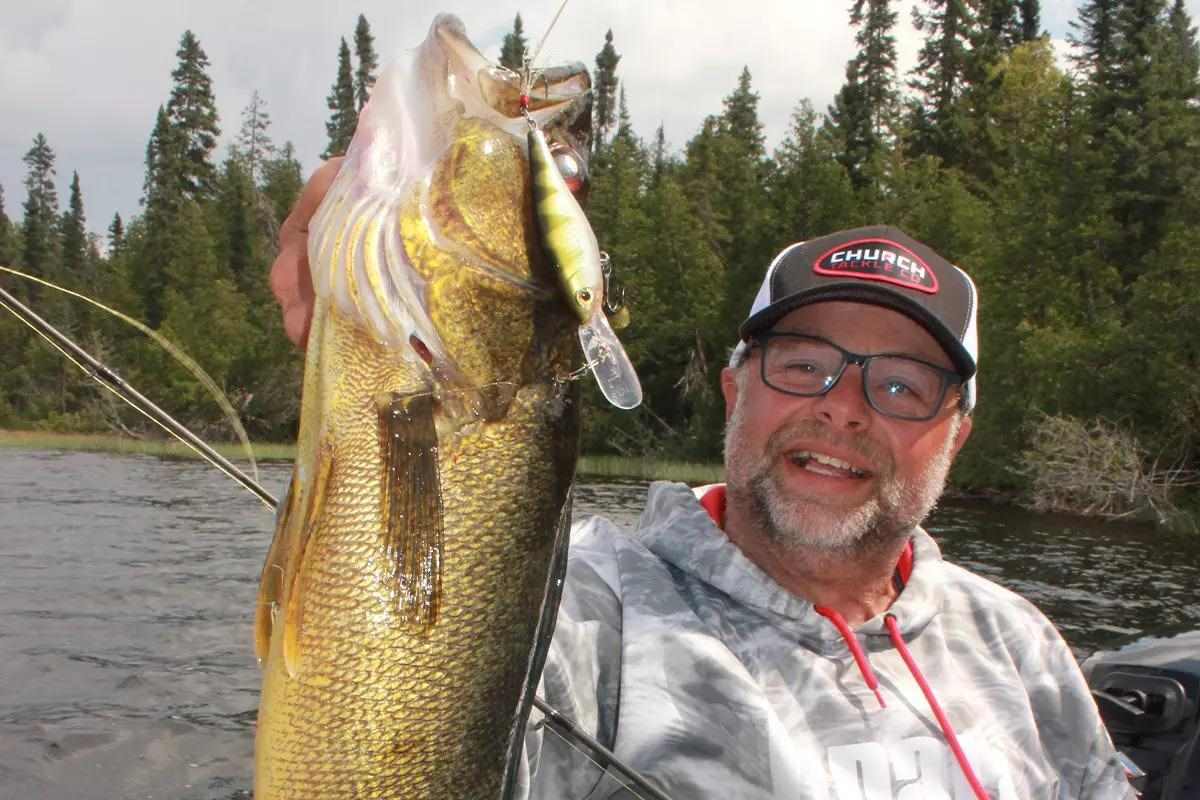 An angler holds up a walleye with a crankbait hanging from its mouth. 
