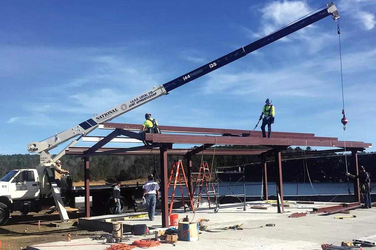 A pickup with a crane hoists building materials as workers build out a building's frame. 