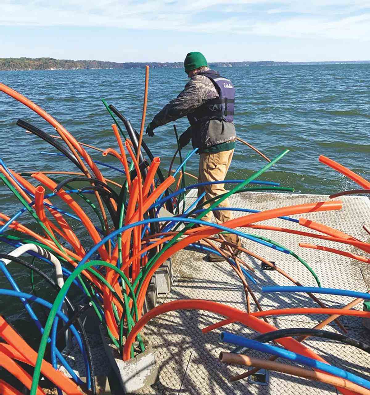 Various-colored small plastic tubes. called spider block fish attractors, next a man wearing a PFD on a dock on water.