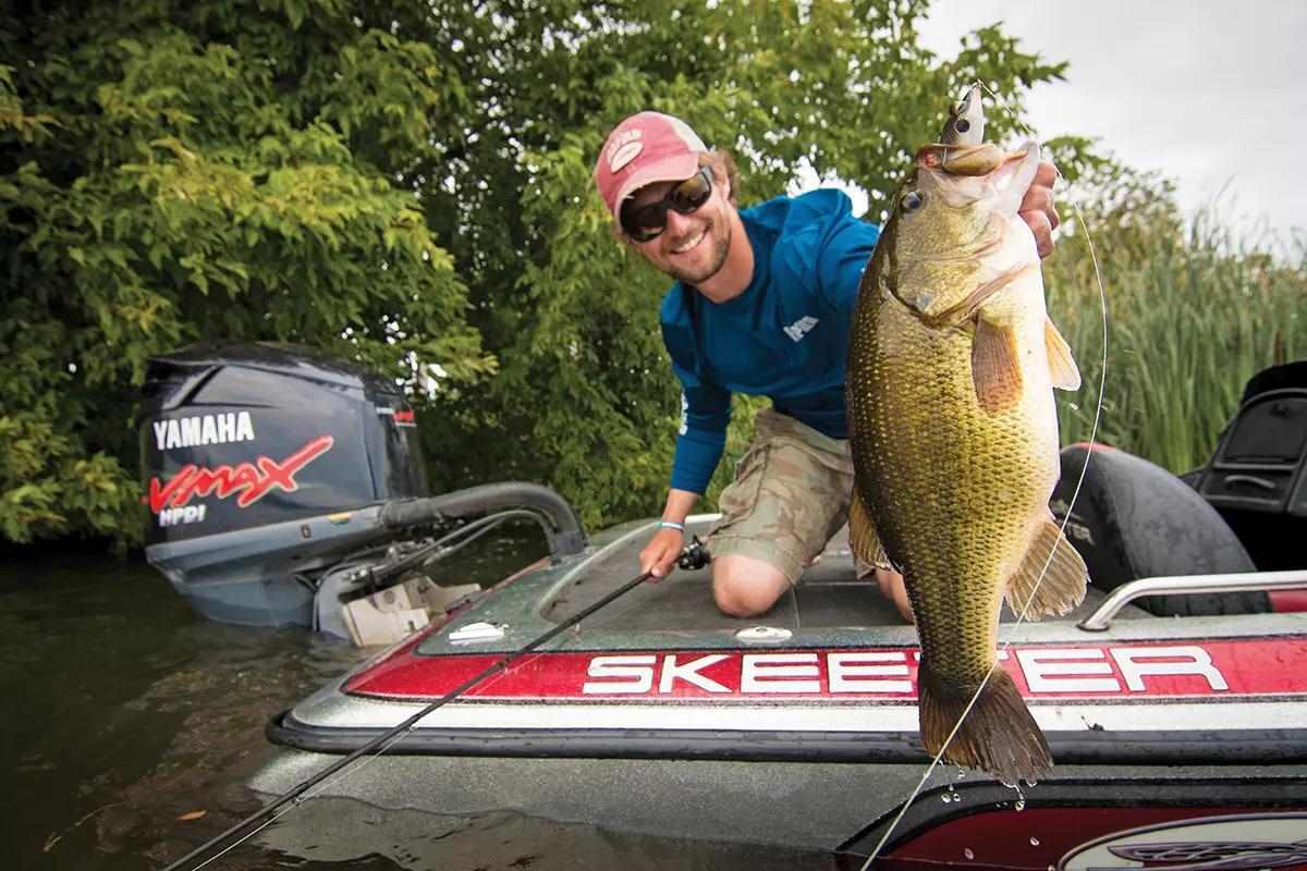 An angler in a boat holding a large largemouth bass for the camera.