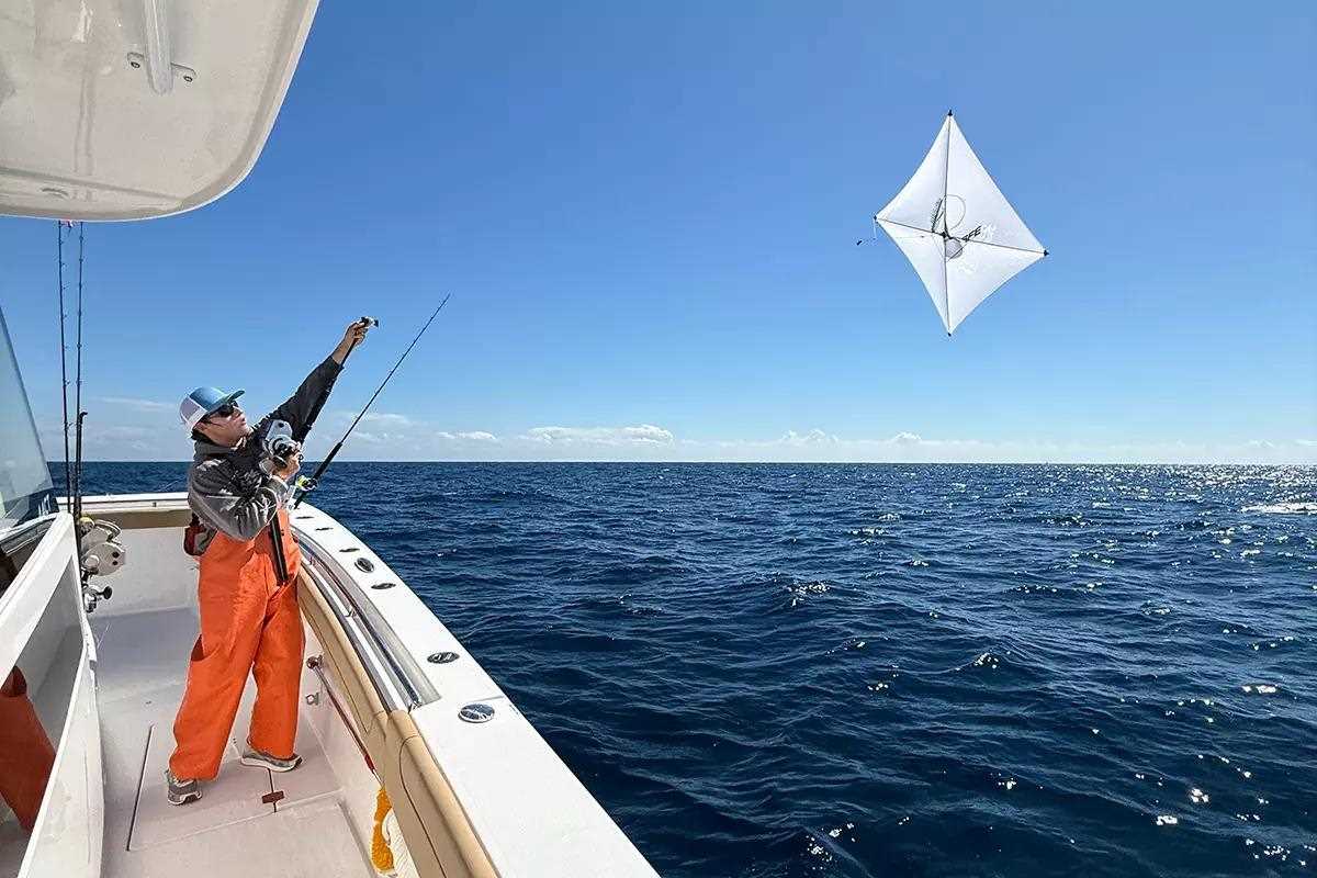 Man in orange foul weather overalls hold line with white fishing kite