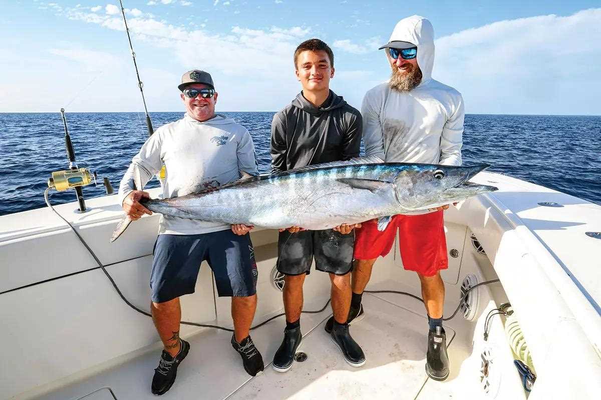three men hold up a large wahoo on a fishing boat