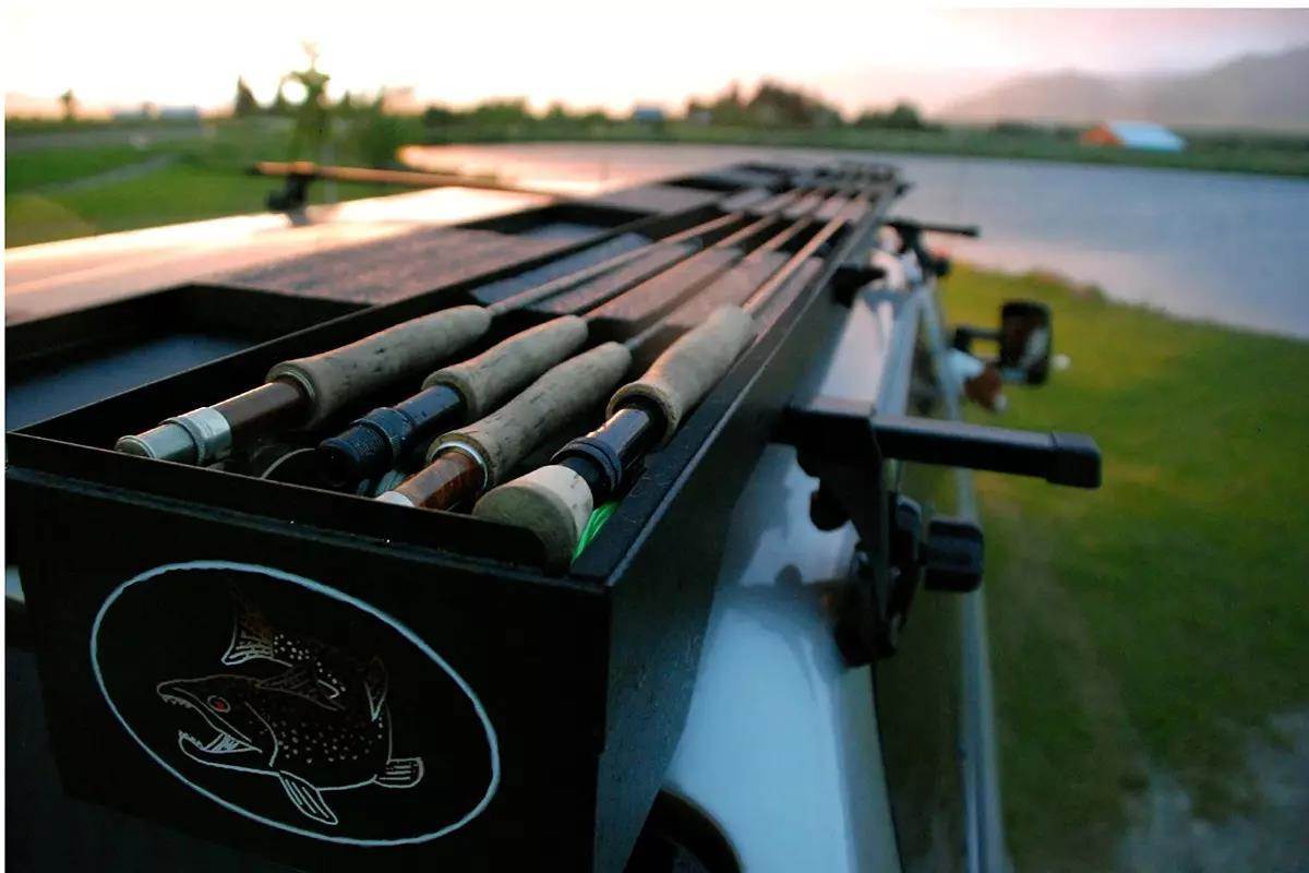An open Big Sky Rod Box roof-top fly-rod carrier next to a river at sunset.