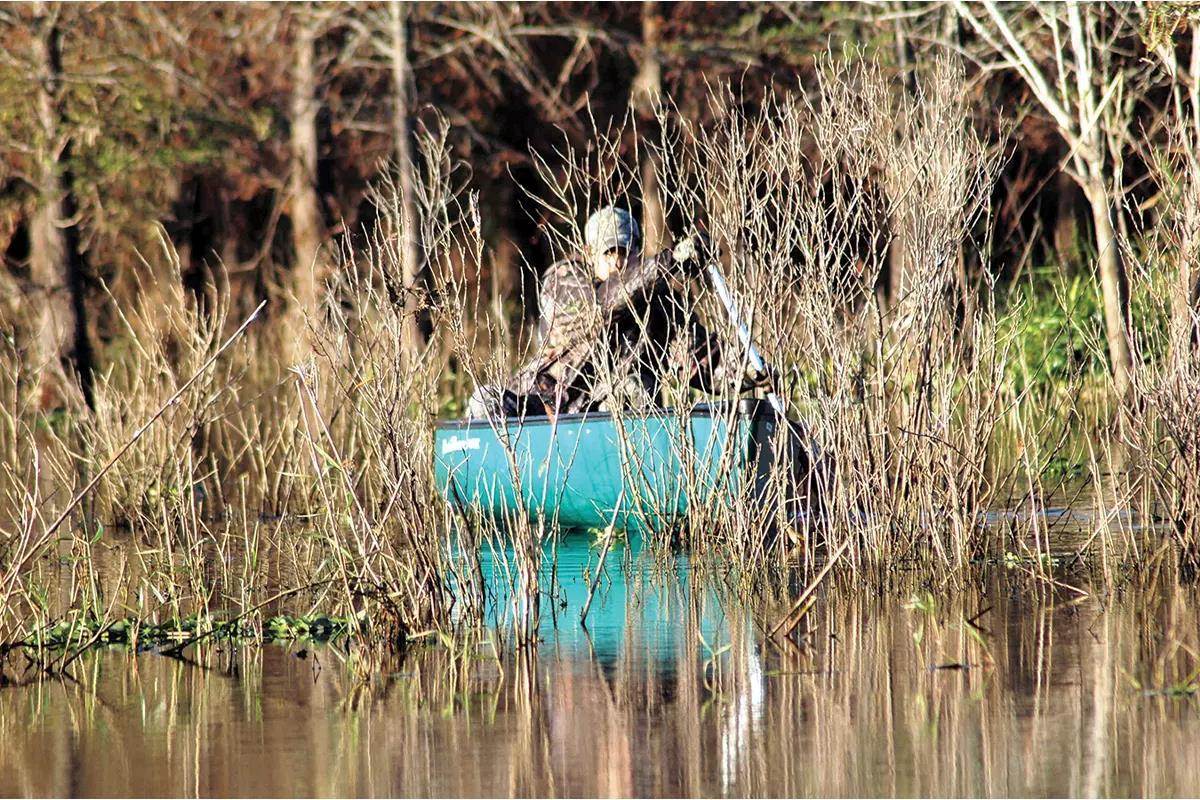 A hunter paddles a boat through some vegetation. 