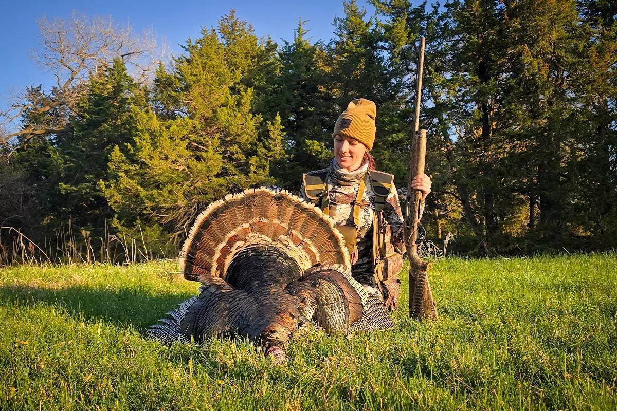 female hunter holding shotgun and admiring her turkey harvest