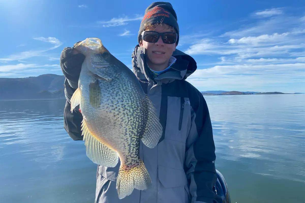 A youth angler holds up a sizable crappie while in a boat. 