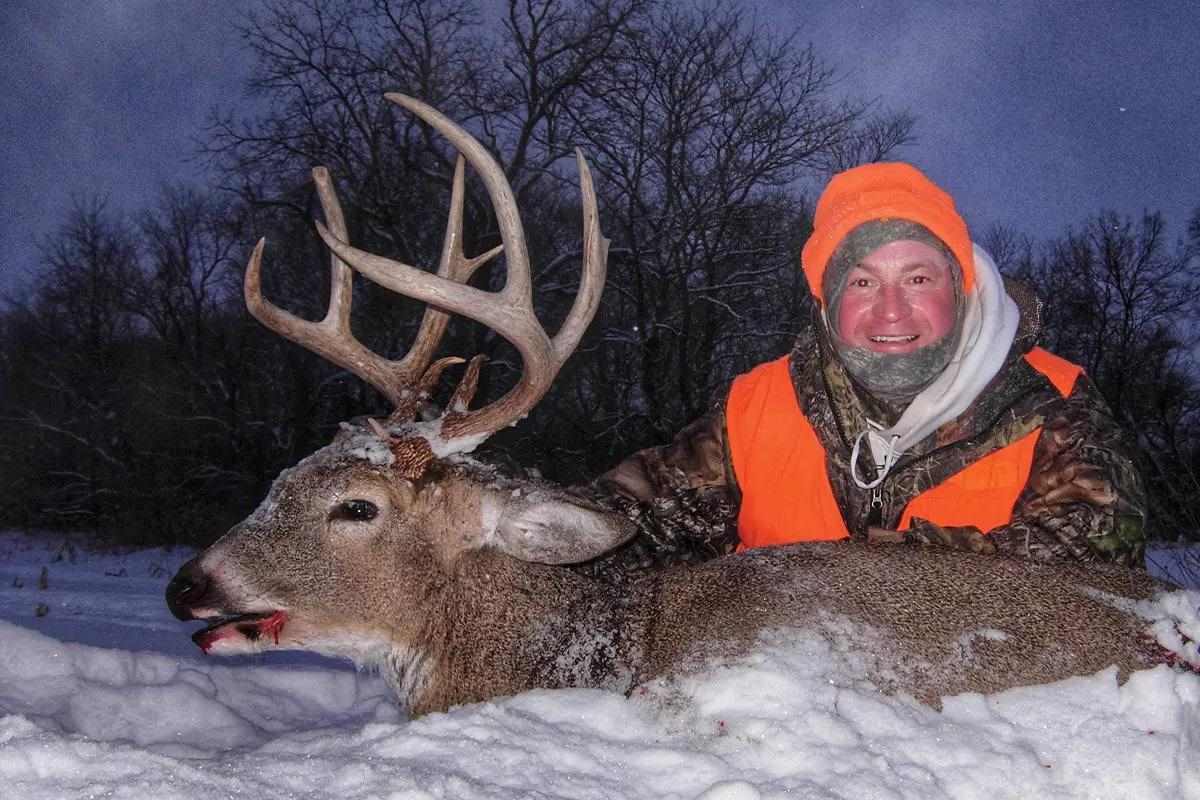 A hunter poses with a harvested buck in the snow. 