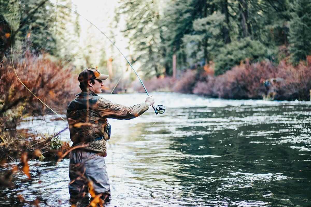 fly fisherman casting into a stream surrounded by colorful foliage