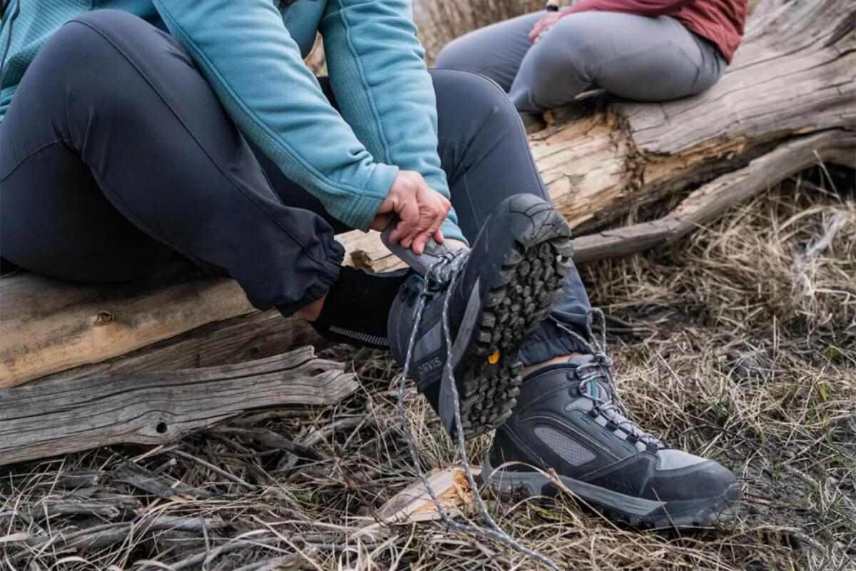 woman sitting on downed tree while tying Orvis Ultralight Wading Boot 