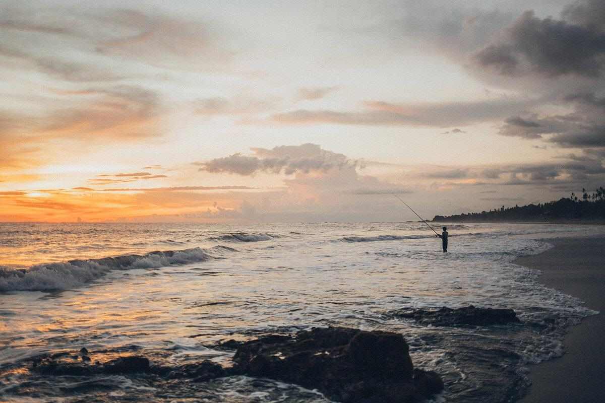 sunrise at the beach with rocks and a fisherman near the water line