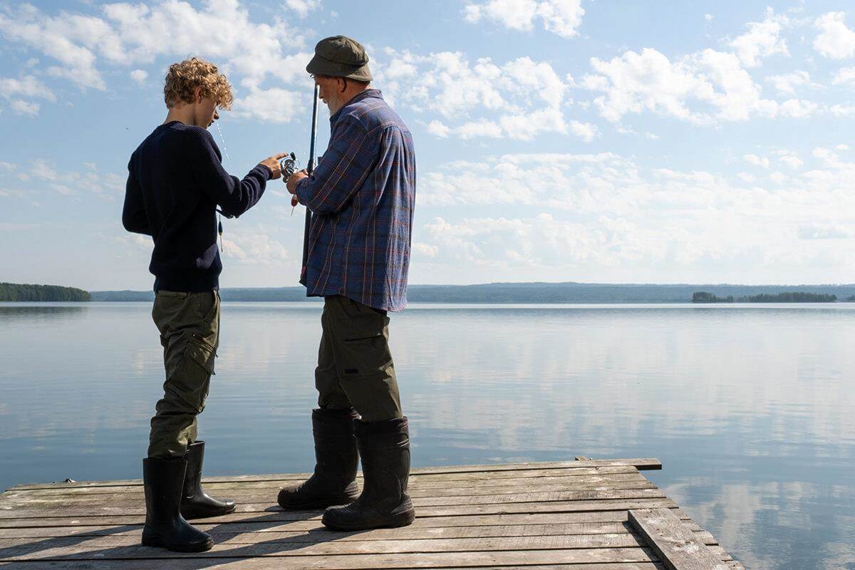 grandson and grandfather looking at fishing rod near a lake