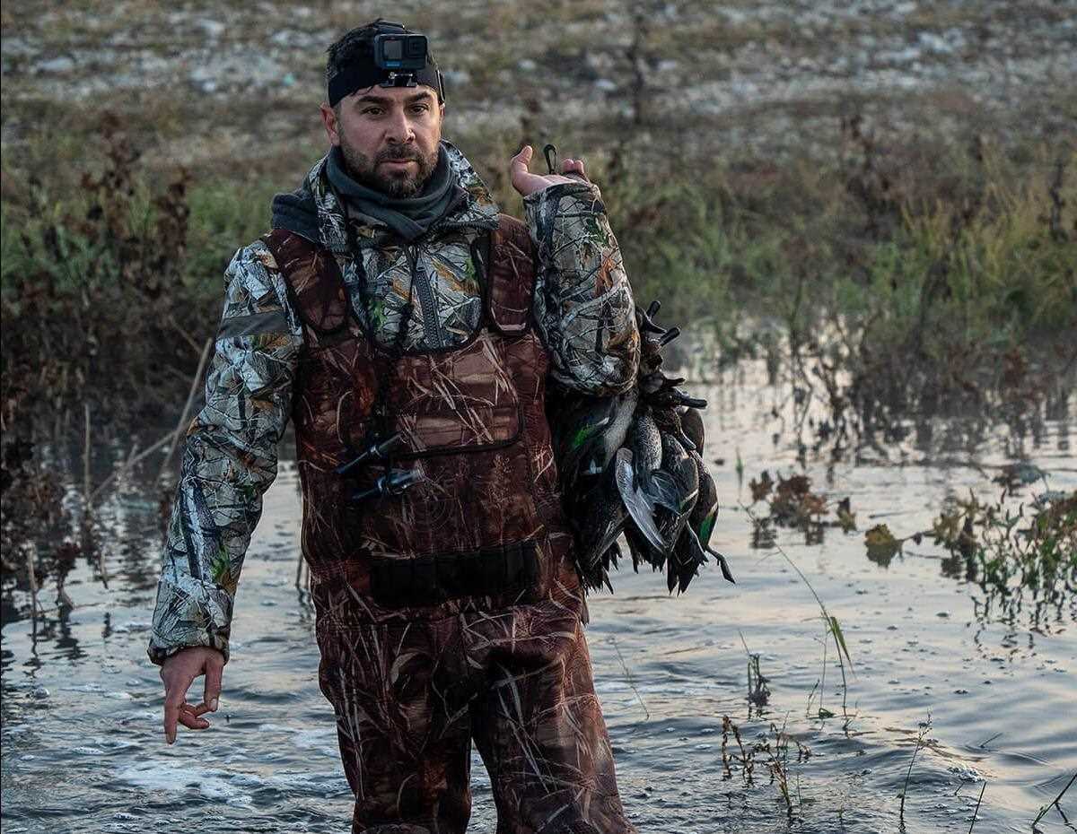 hunter walks towards camera with a full string of ducks