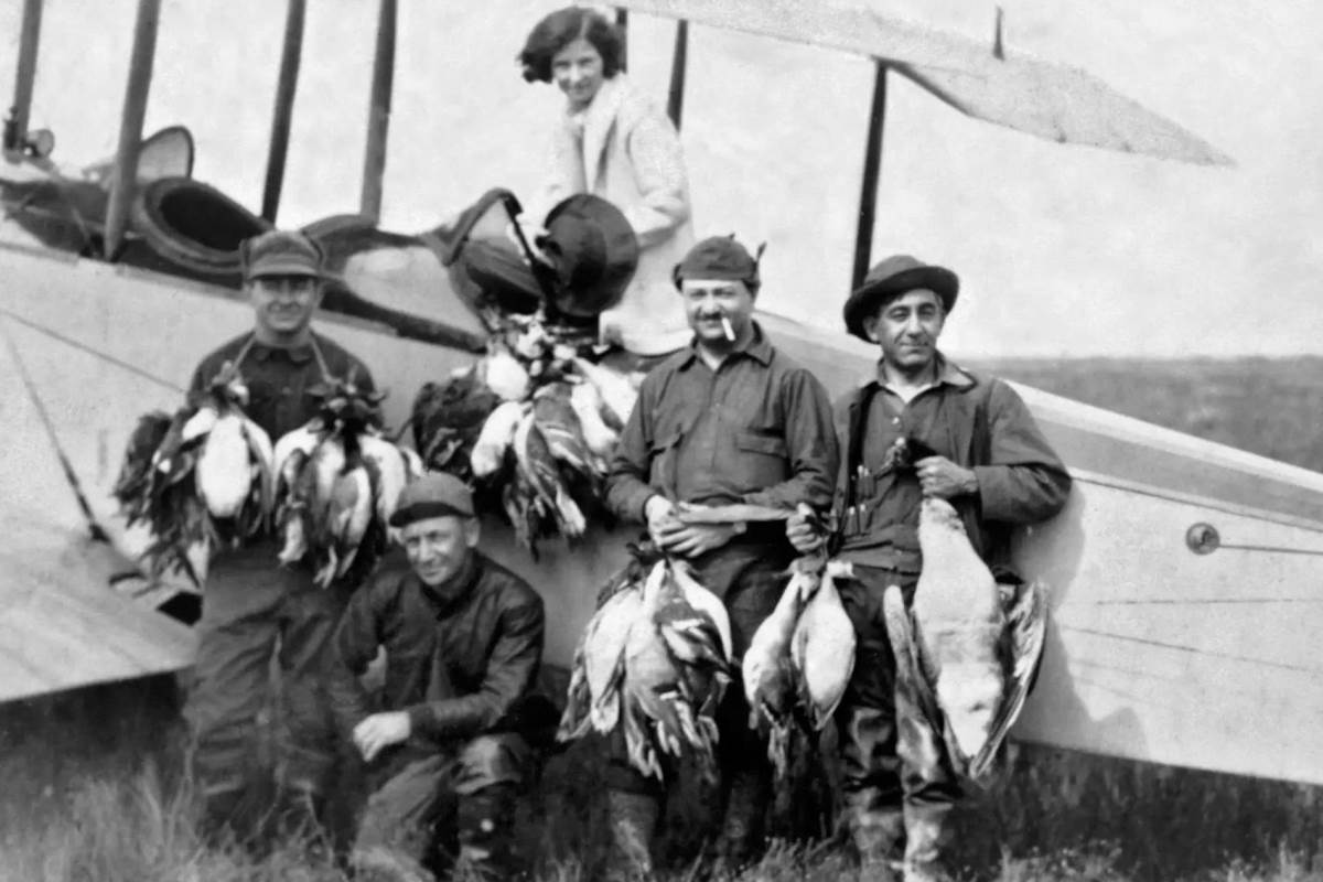 Hunters posing with ducks in front of their plane.