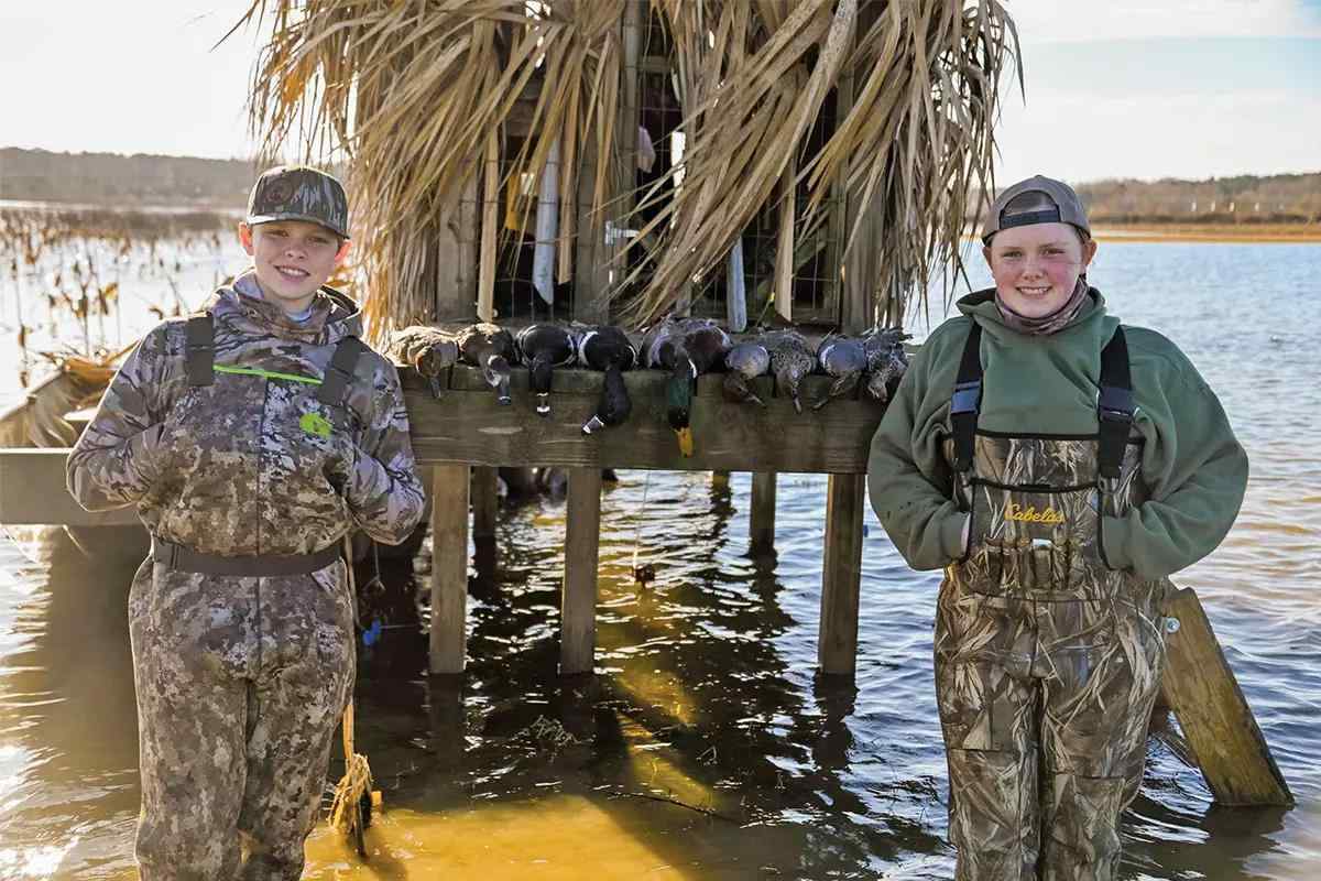 Two youth duck hunters stand in the water next to a line of ducks.