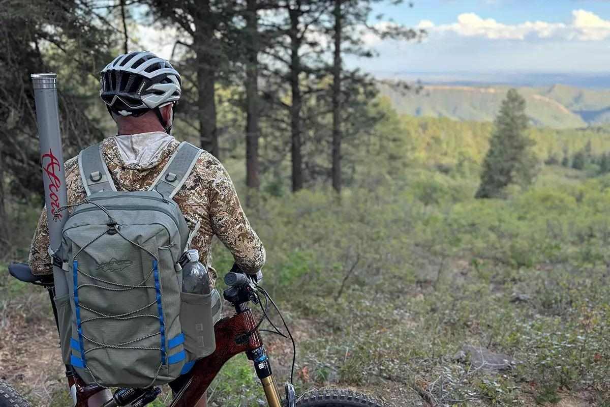 A man on an e-bike stopped to admire a mountain view, with a fly rod and pack on his back.