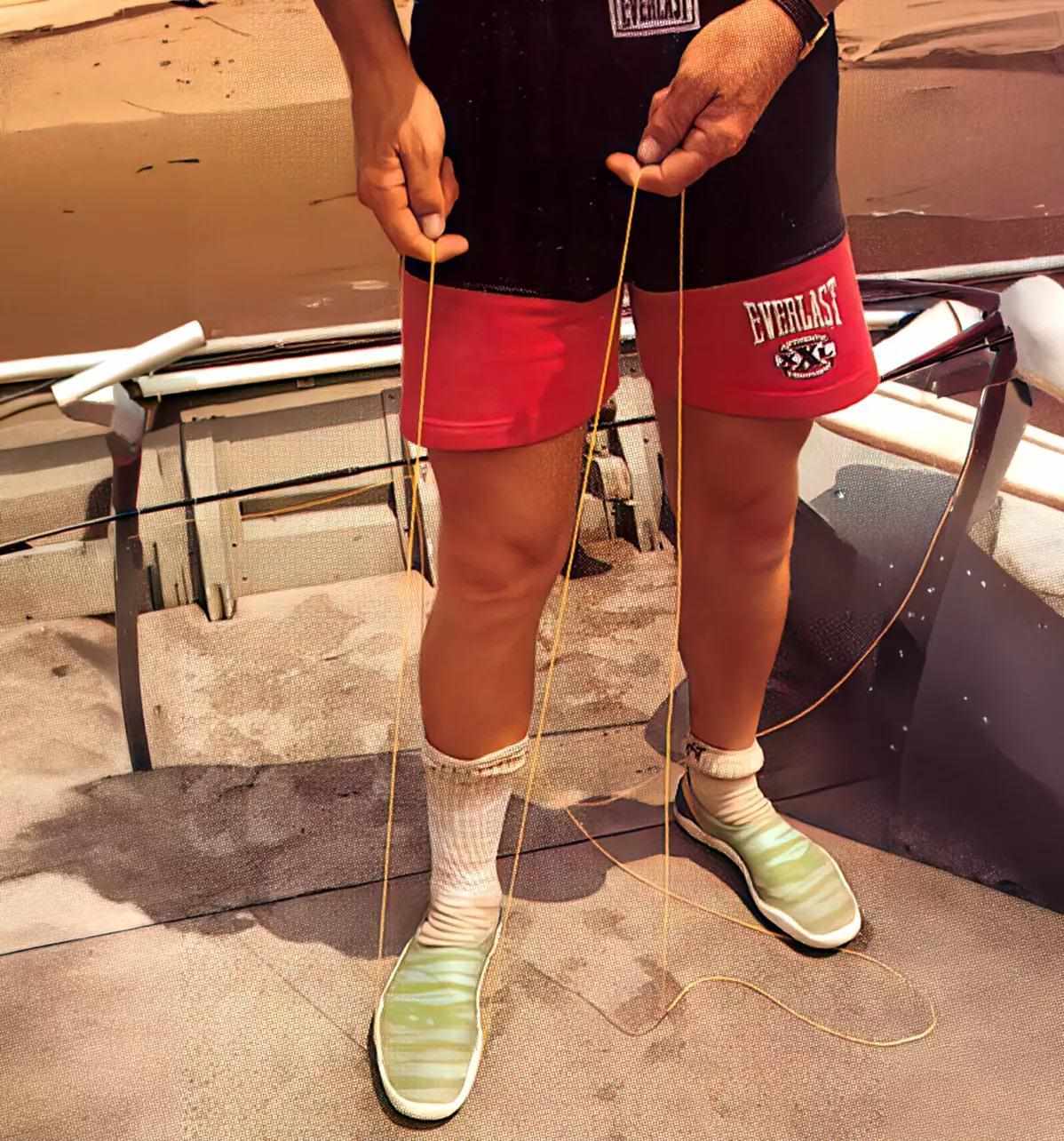 The torso and legs of a man stepping on a fly line to stretch it out with his hands.