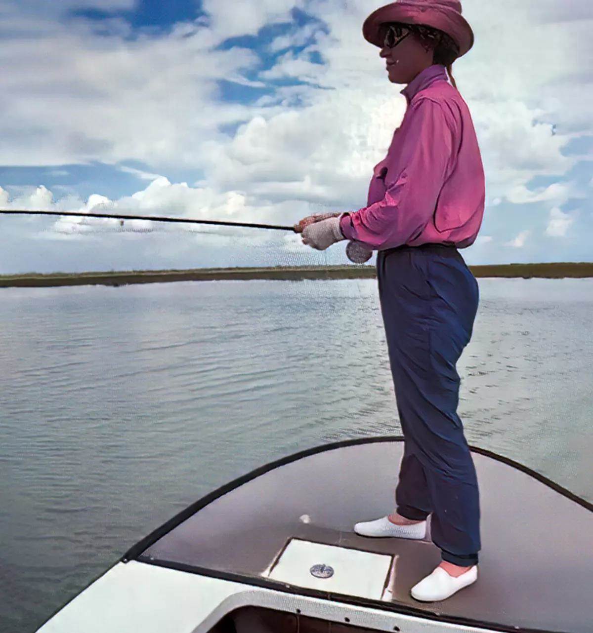 A fly angler standing on the deck of a flats boat watching for bonefish.