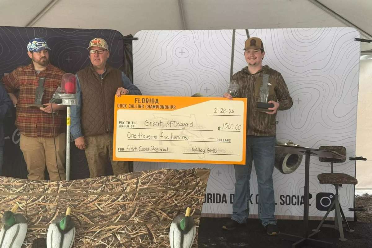 A duck caller with a check and a trophy.