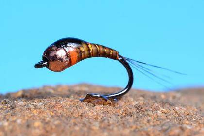 A Perdigon nymph displayed on a rock; a closeup of a fly-fishing fly.