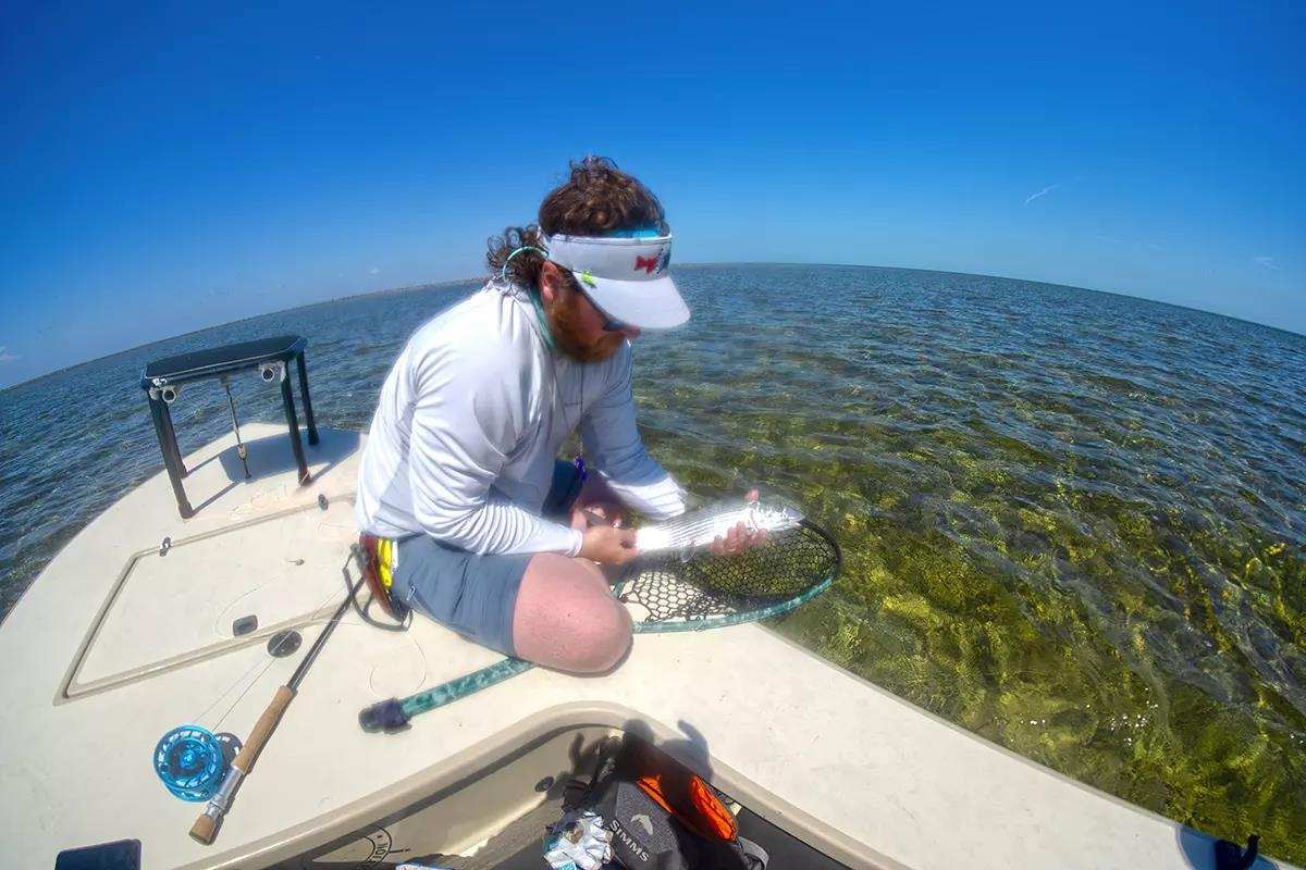 A fly angler on a flats boat holding a bonefish. 