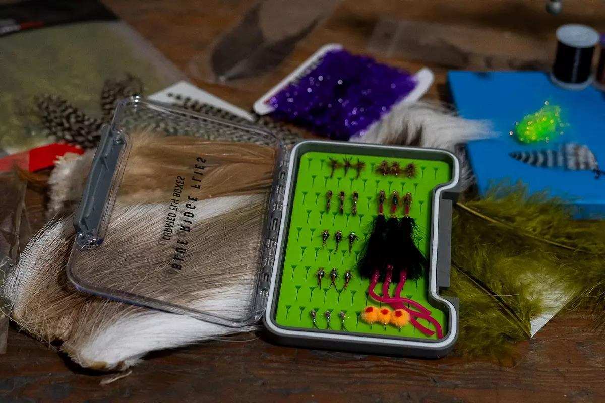 A slim fly box on a table next to fly-tying materials. 