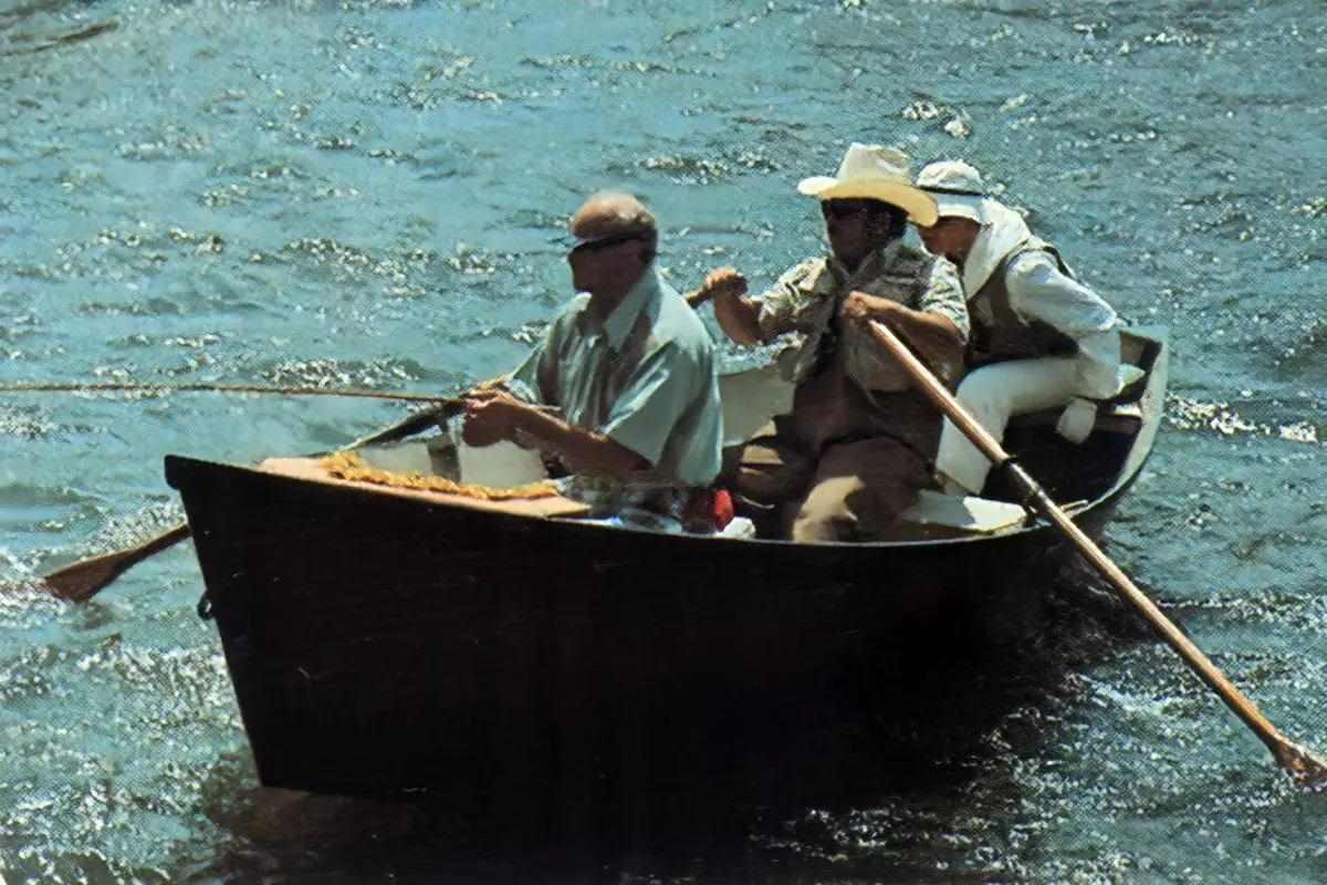 Three people in a drift boat on a river. 