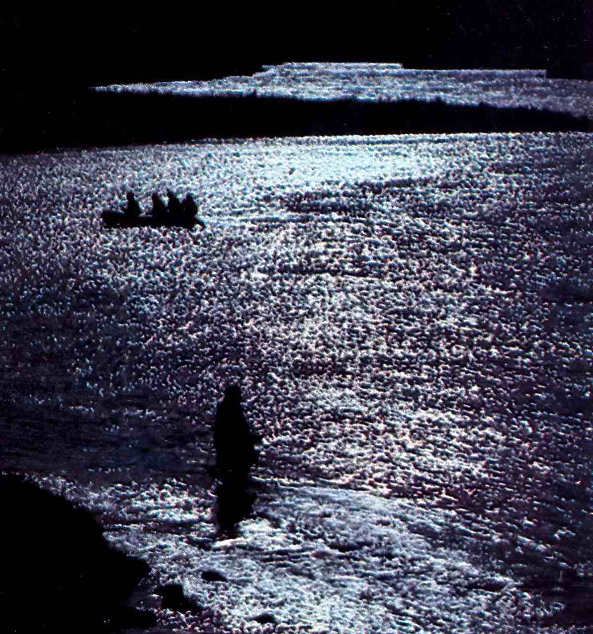 A fly angler wading in a river in the foreground with a raft full of anglers in the background; all are silhouetted against the sheen of a river.