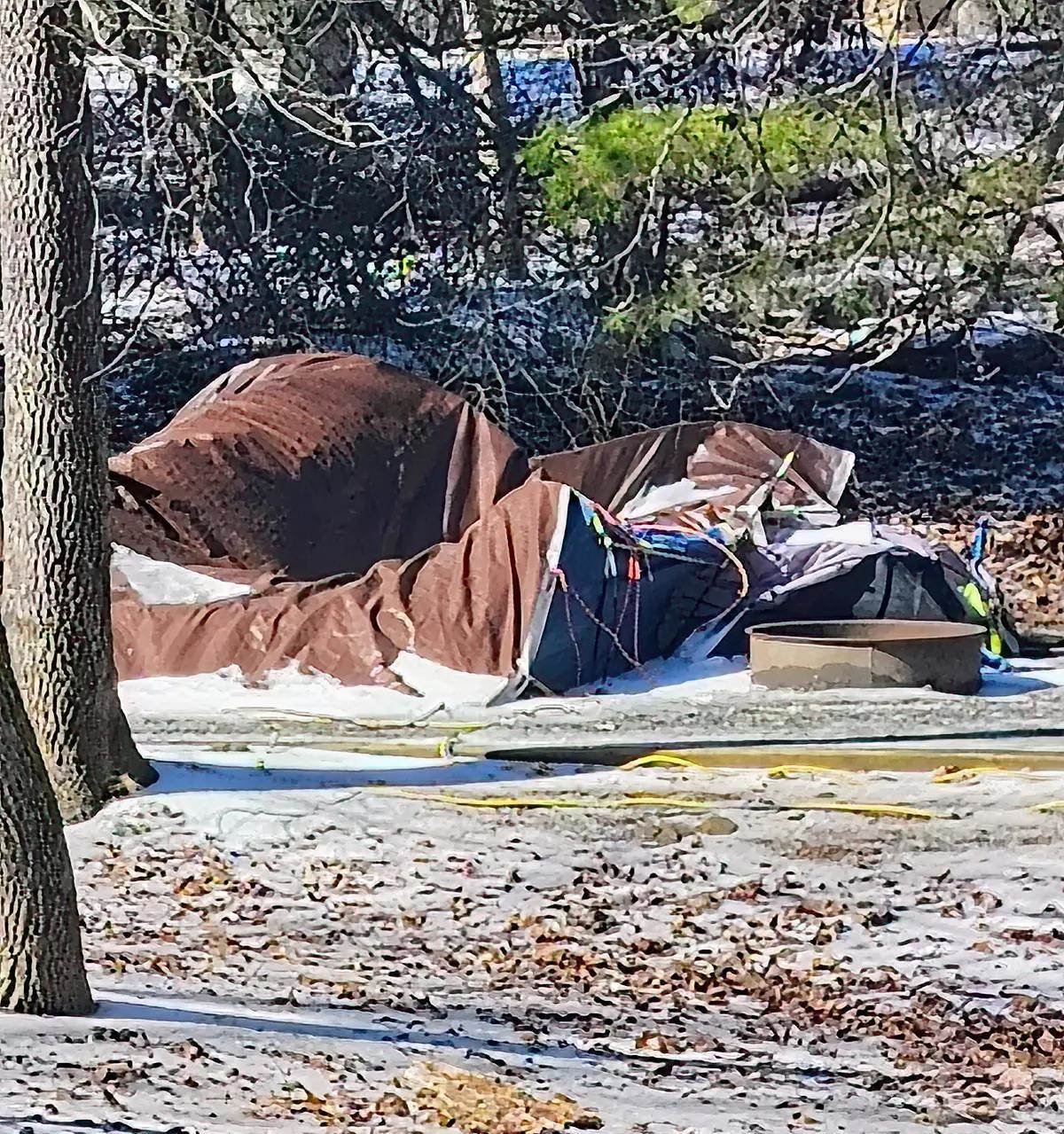 A pile of tarps and bungee cords next to a fire ring near some pine trees.