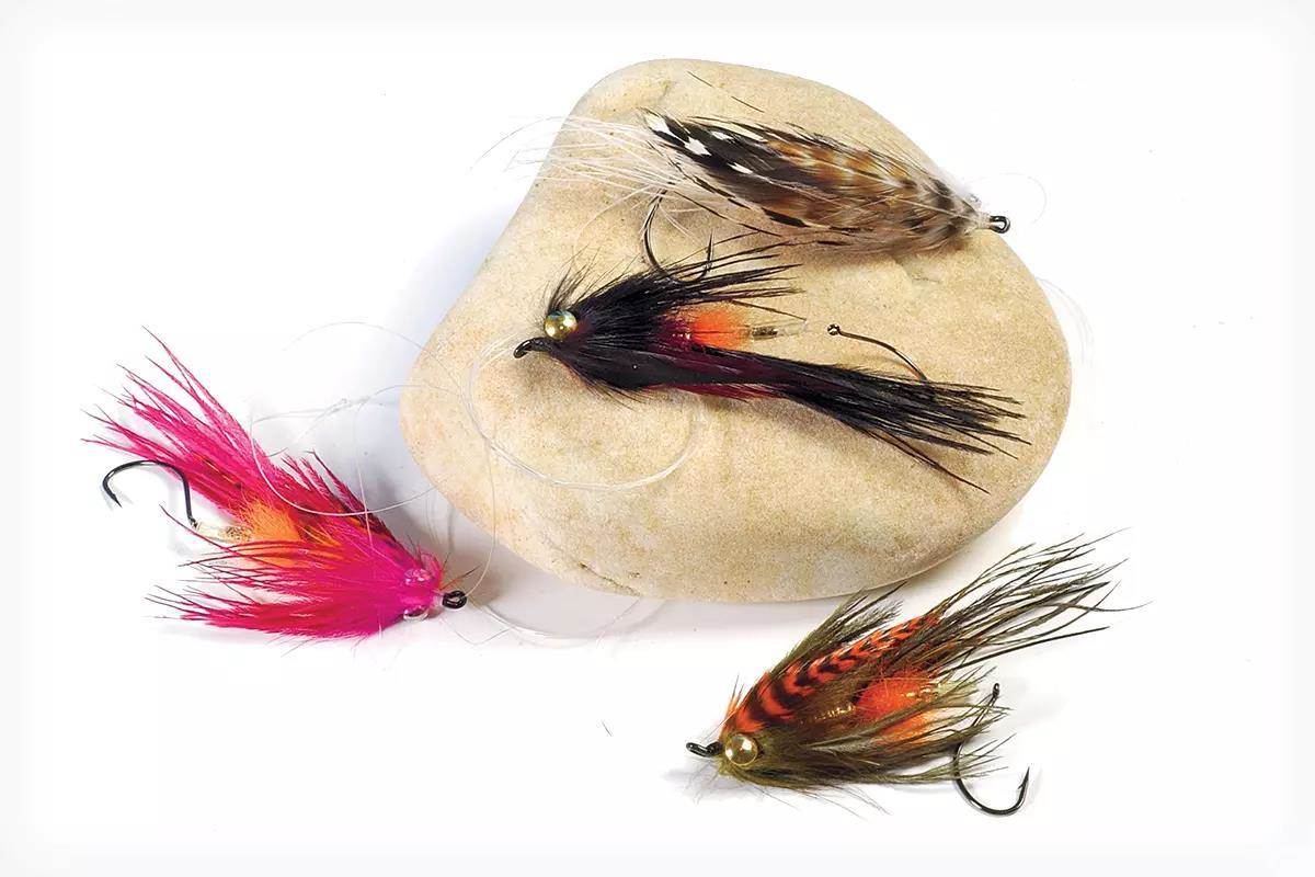 Four large colorful steelhead flies placed around a rock on a white background.