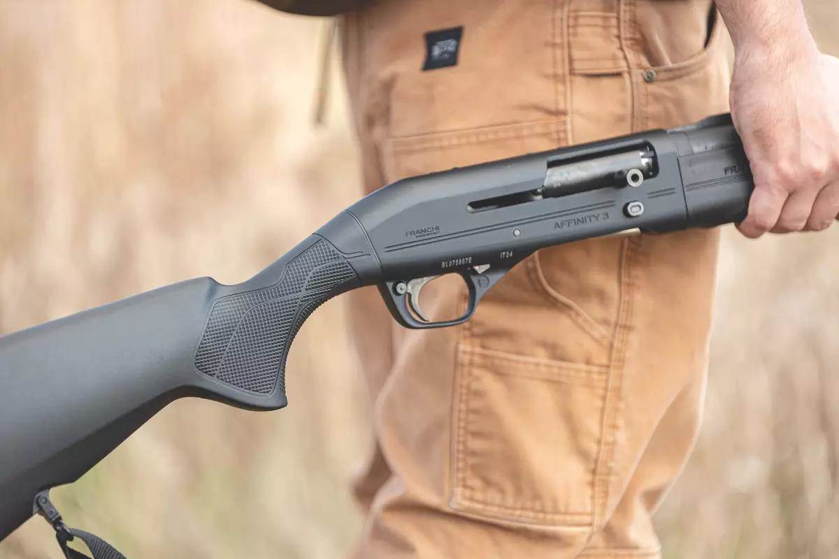 A hunter carries a shotgun in his right hand. 