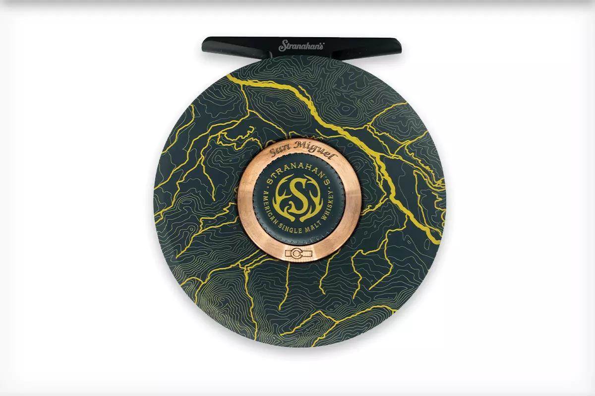 A green fly reel with a river map pattern etched on it. 