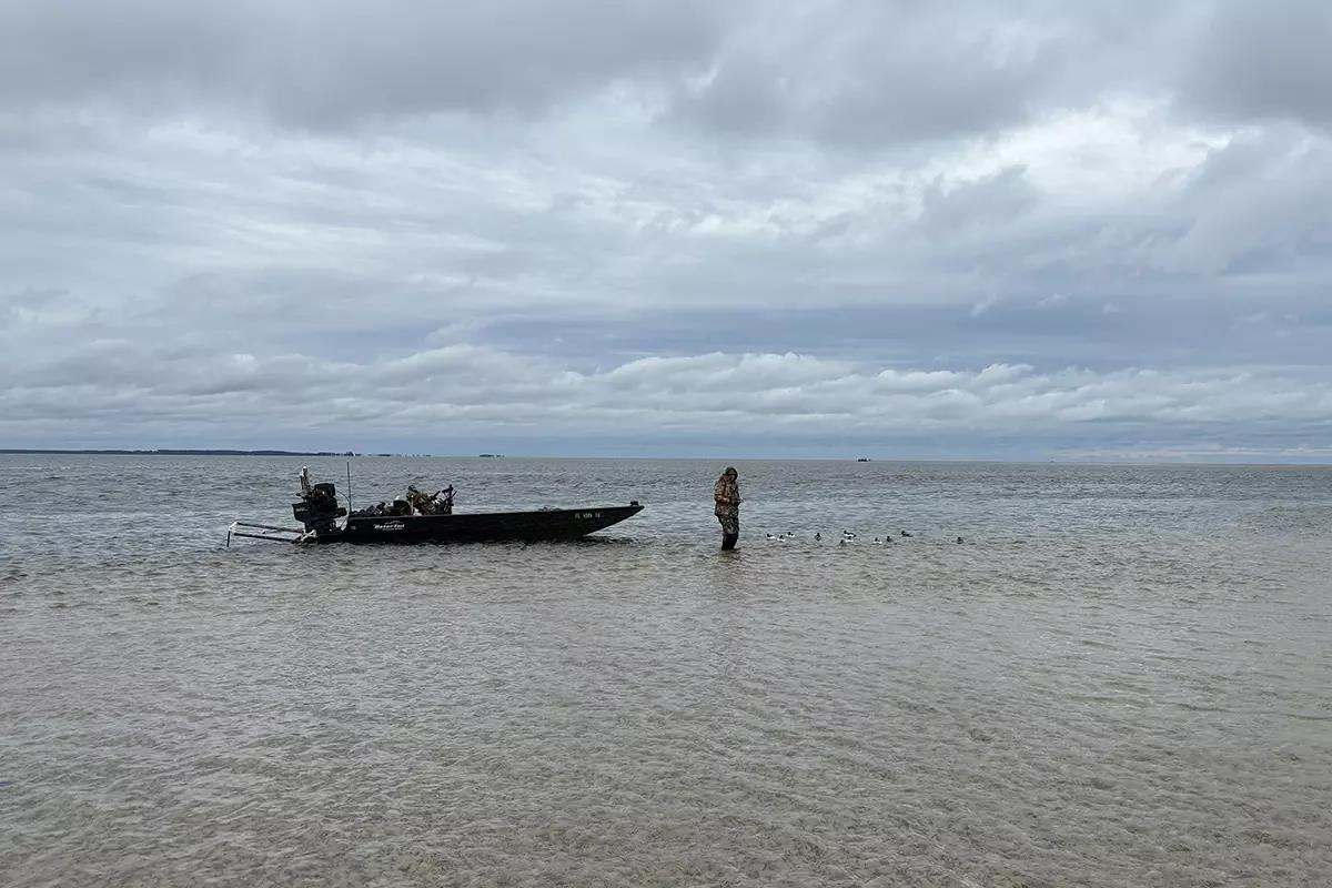Wade fisherman pulls boat in shallow water.