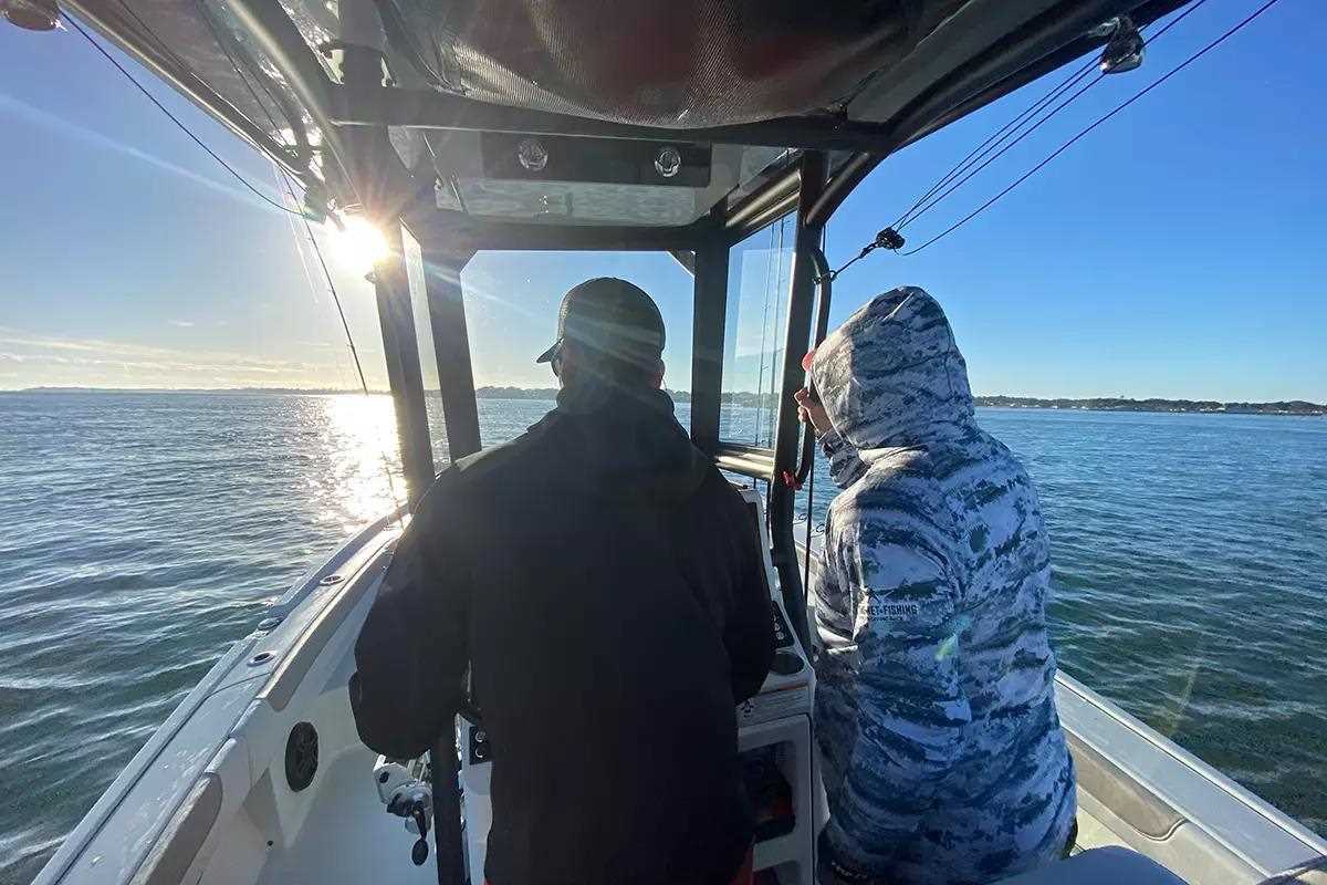 two men at helm of boat running into sun