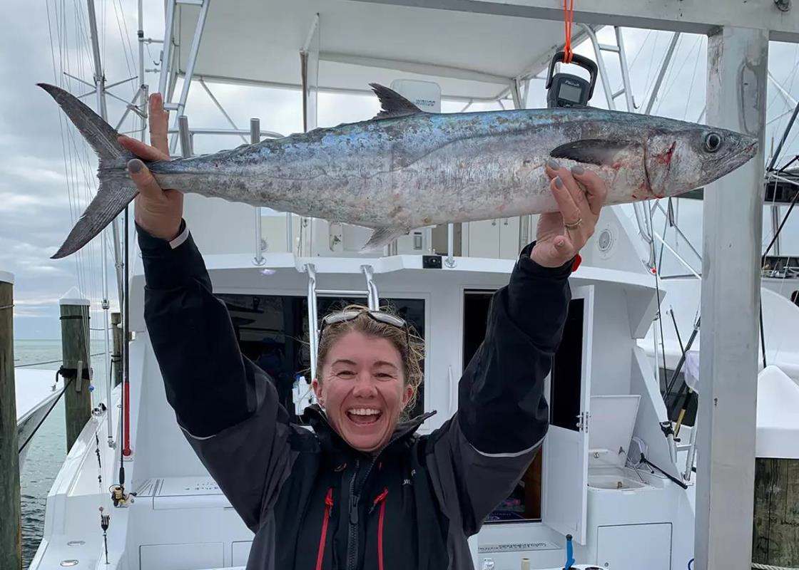 Woman holds large king mackerel overhead at dock behind boat