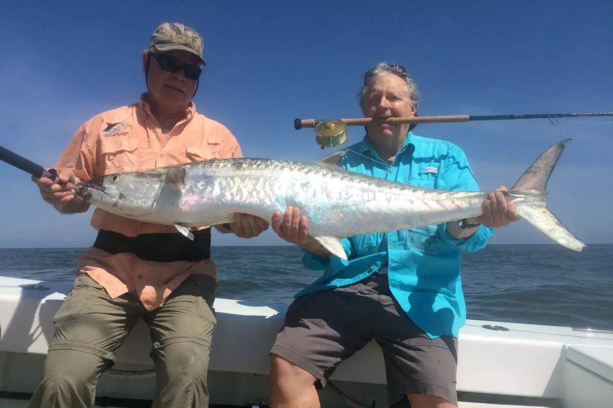two men hold large king mackerel man in blue shirt has flyrod in his mouth