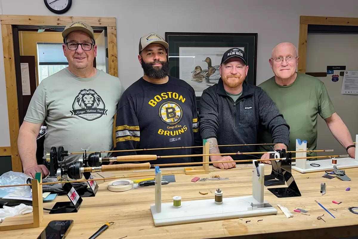 Four men smile for camera behind a table that holds some bamboo-fly-rod-building equipment.